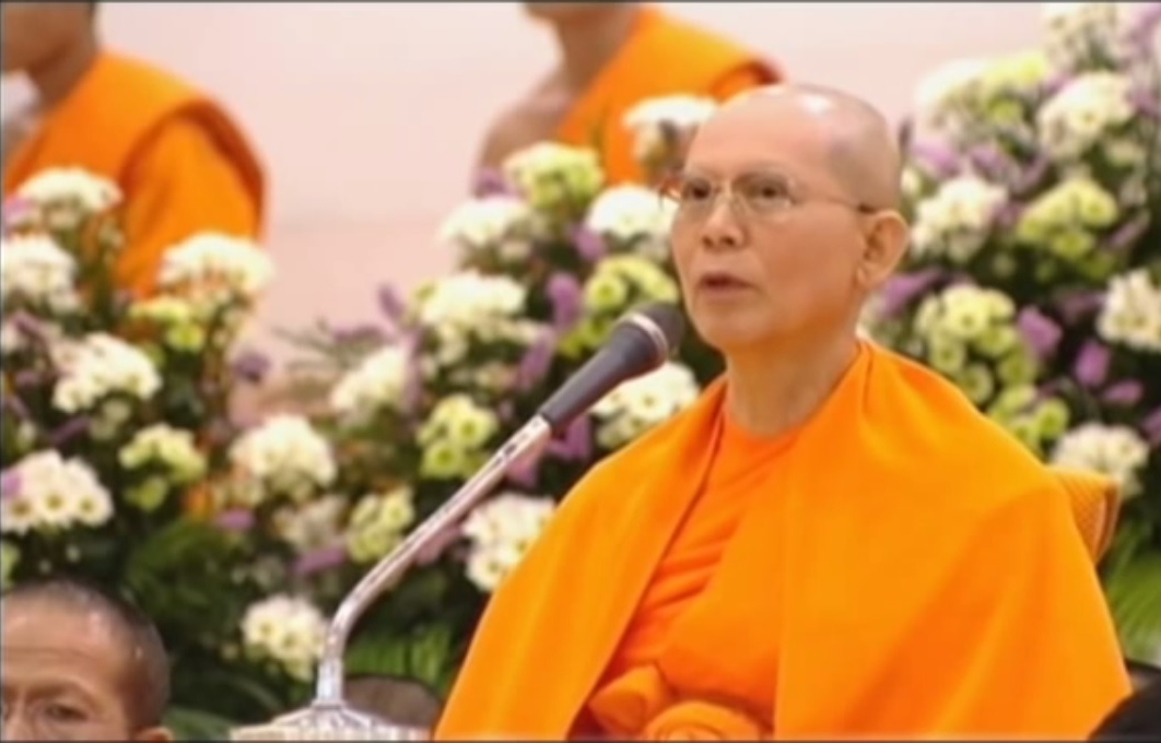 Luang Por Dhammajayo speaking with flowers behind him